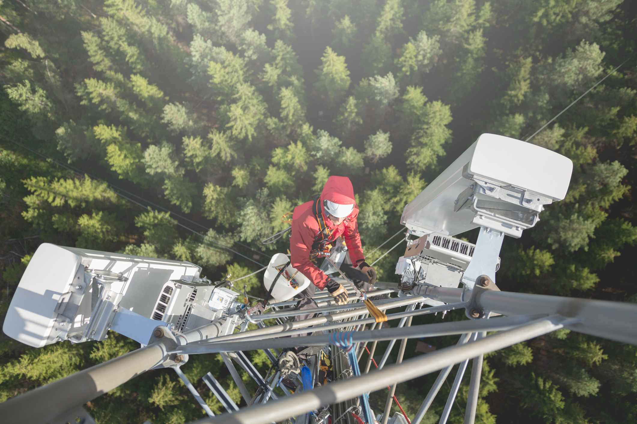 Telecommunication manual high worker engineer installing new 3g 4g LTE antenna on tall mobile base station (communication tower) in the middle of european forest, high angle of view. Working at height. Telecommunication masts and towers are typically tall structures designed to support antennas for telecommunications and broadcasting. Drone point of view.